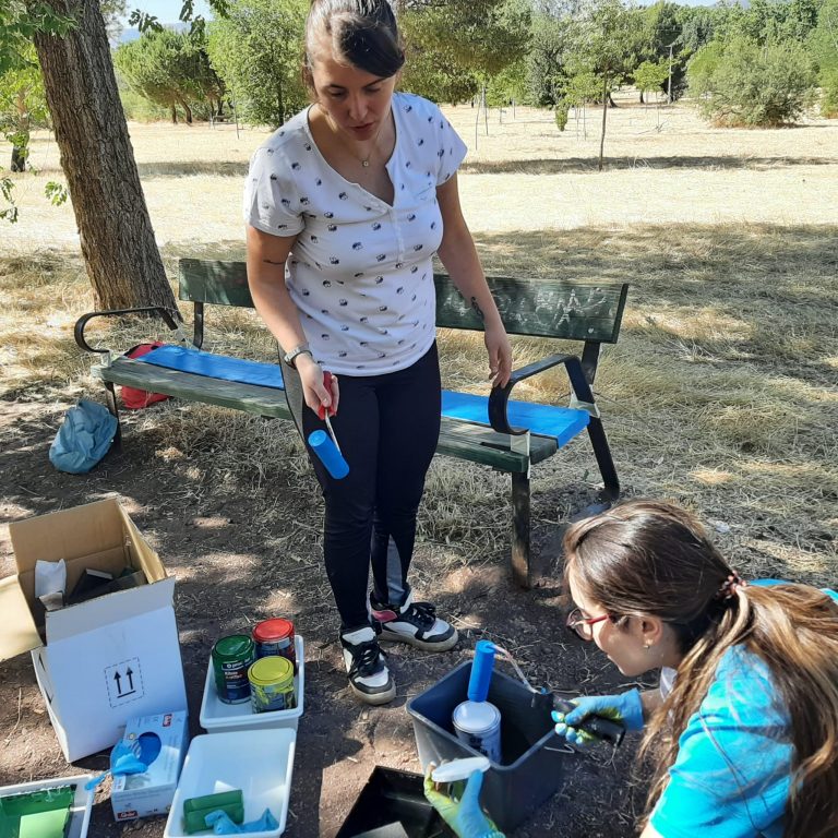 Chicos y chicas de Cruz Roja pintan los bancos del parque Pozo Norte de Puertollano